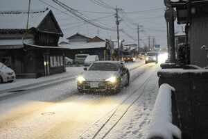 積雪の中、ライトをつけて走行する車＝８日午前７時ごろ、佐賀市久保田町