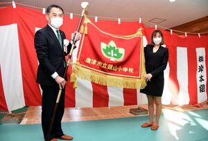 新校舎完成に合わせ新しくなった校旗を披露する峰達郎市長と、寄贈した都建設工業の稲田美知子取締役