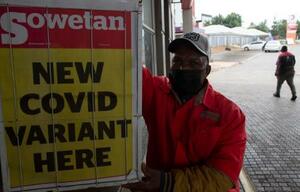 　南アフリカで新型コロナウイルスの新たな変異株の出現を伝える新聞見出しの看板の横に立つ給油所のスタッフ＝２７日、プレトリア（ＡＰ＝共同）