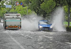 冠水した道路の上で、高い水しぶきをあげながら進む乗用車＝１４日午前７時半ごろ、佐賀市の城内通り