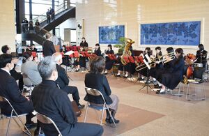 演奏をする佐賀商高吹奏学部の生徒らと、演奏に聴き入る職員ら＝県庁新館１階の県民ホール