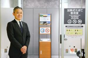 　函館空港ビル内にある加熱式たばこ専用の喫煙所の前に立つ八島聡社長＝１日午前